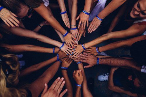 Diverse group of people put their hands together in a circle to embody teamwork